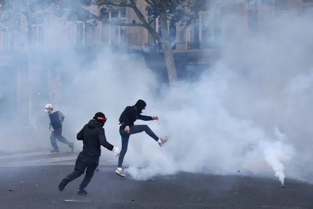 Un manifestante enmascarado intenta patear un bote de gas lacrimógeno en medio de enfrentamientos con la policía antidisturbios francesa durante una manifestación contra el coste de la vida y el aumento de los precios del combustible en la plaza de la República de París, como parte de las protestas nacionales convocadas por el movimiento de los chalecos amarillos, a las que se sumaron estudiantes franceses de secundaria y universitarios, profesores y padres que exigen mejores condiciones escolares