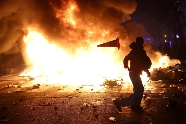 Un hombre arroja un cono de tráfico de plástico a través de una barricada en llamas en medio de enfrentamientos durante una jornada de manifestaciones contra el coste de la vida y el aumento de los precios del combustible en París, como parte de las protestas nacionales convocadas por el movimiento de los Chalecos Amarillos, a las que se unieron estudiantes de secundaria y universitarios, profesores y padres franceses que exigían mejores condiciones escolares y medidas gubernamentales, así como sindicatos